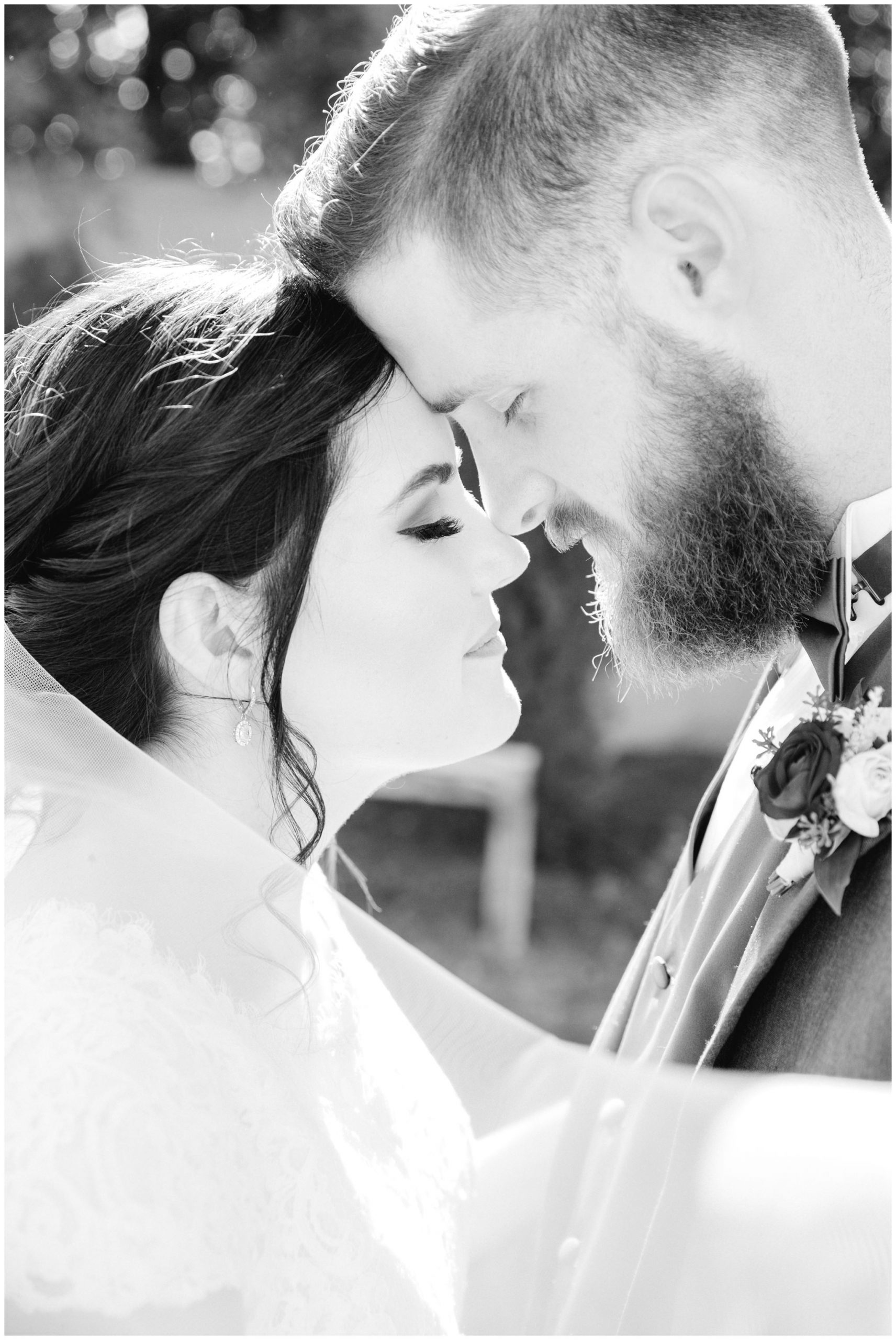 Black and white image of bride and groom snuggling close together at their wedding about to kiss.